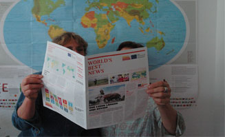 Zwei Personen lesen Zeitung vor einer Weltkarte